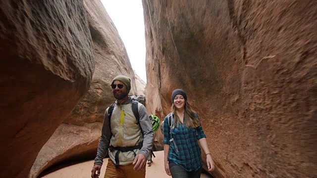 一群带着狗的朋友在摩押徒步旅行中穿过狭窄的狭缝峡谷时互相微笑。视频素材