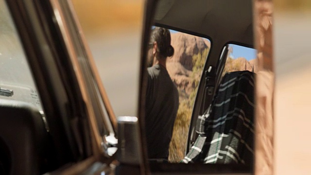 铜。年轻男子在副驾驶座的后视镜中，抬头望着山，然后下车。视频素材