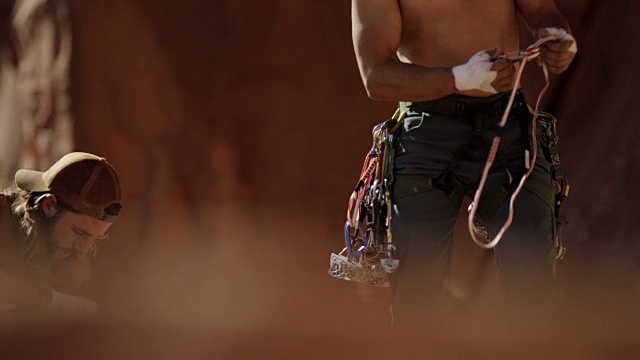 一个年轻人带着登山装备和挽具仰望着壮观的岩壁。视频素材