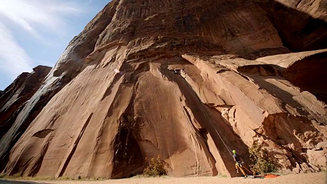 当攀岩者攀登雄伟的砂岩岩壁时，保护者放松绳索。视频素材