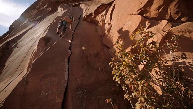 当保护者从下面观看时，登山者沿着岩石表面的绳索在砂岩上投下阴影。视频素材