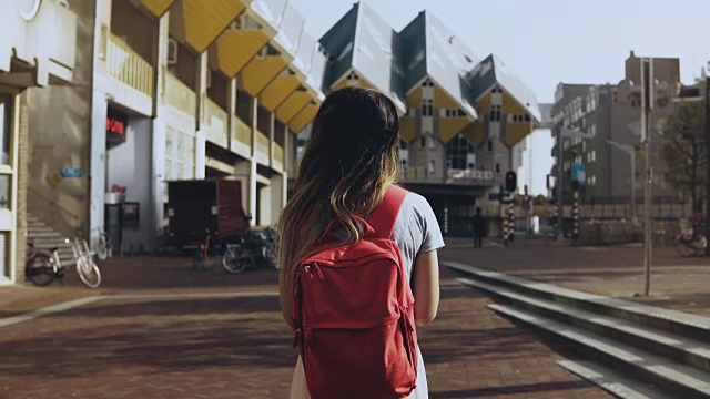 长头发的女孩走过美丽的建筑。欧洲当地女子，红色背包。鹿特丹Cube House, 4K视频素材