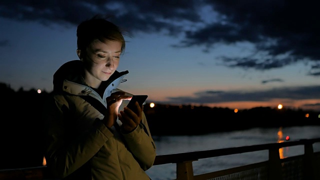 一名女子晚上在游轮甲板上使用垂直智能手机视频素材
