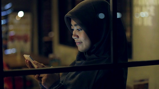 一名戴着头巾的东南亚穆斯林妇女正在用手机浏览互联网视频素材