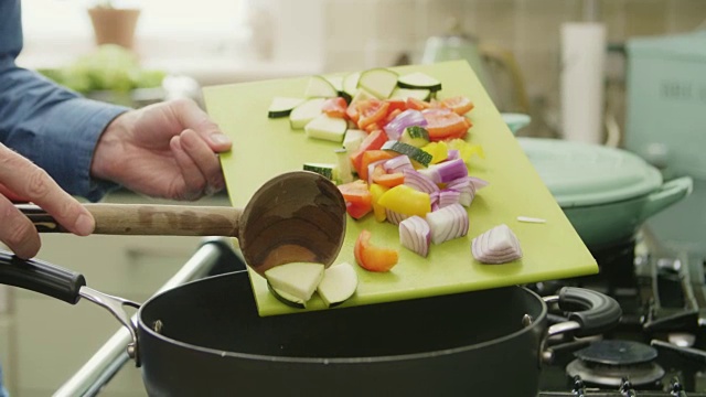 一名男子用勺子在平底锅中加入新鲜蔬菜视频素材
