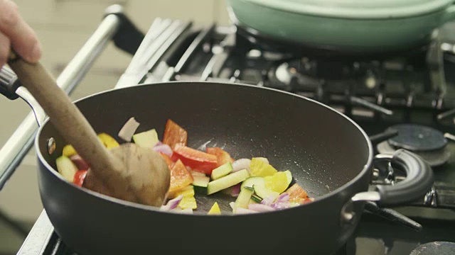 男子用平底锅在炉子上炒多种颜色的蔬菜视频素材