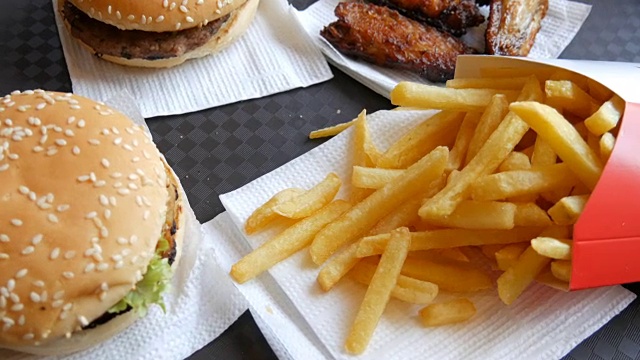 托盘上是快餐。不健康的食物在桌子上汉堡包，炸薯条和炸鸡翅视频素材