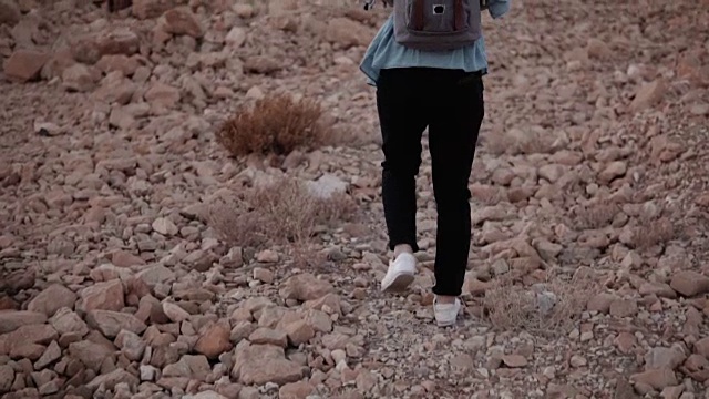 在沙漠的巨石上徒步旅行的女孩。缓慢的运动。一位女性旅行者拿着大石头爬上了山。困难。以色列视频素材