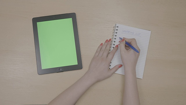 Top视图的女人的手计划购物清单与绿色屏幕平板电脑和书写在记事本上视频素材