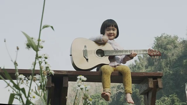 可爱的小女孩在她的休闲活动中，带着积极的情绪，如微笑和有趣的自然花园弹吉他视频下载