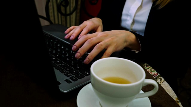 女人的手用一杯绿茶在笔记本电脑键盘上打印文字视频素材