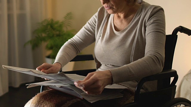 聪明的女人坐在轮椅上看报纸，老年休闲，有空视频素材