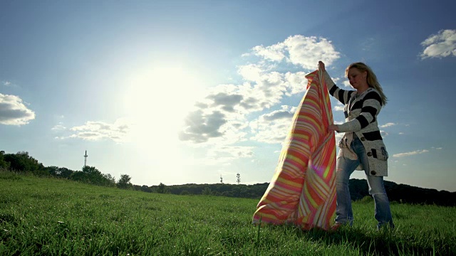 年轻女子在草地上铺开毯子，享受在大自然中放松的一天。视频素材