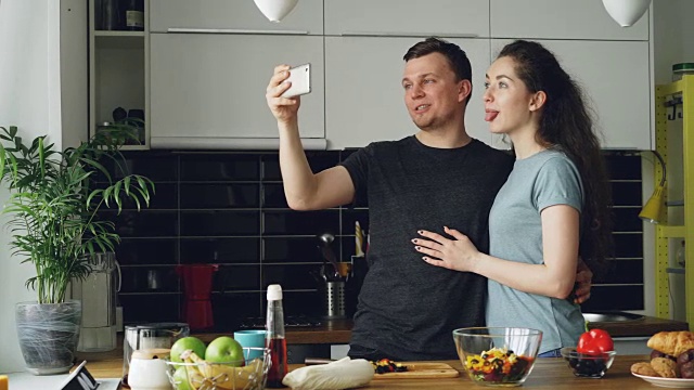 这对年轻有趣的情侣早上在家厨房做饭的时候用智能手机自拍视频素材
