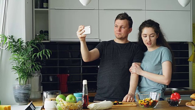一对年轻幸福的夫妇在家里厨房做饭的时候用智能手机摄像头进行在线视频通话视频素材