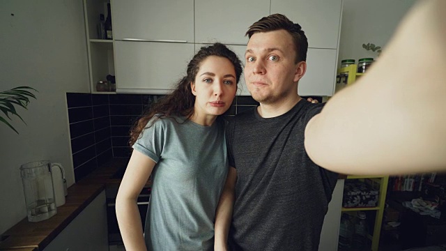 一对年轻有趣的情侣早上站在家里的厨房里用智能手机自拍视频素材