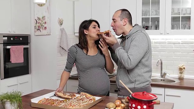 怀孕的妻子和她的丈夫在厨房吃披萨视频素材