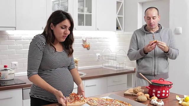 怀孕的妻子和她的丈夫在厨房吃披萨视频素材