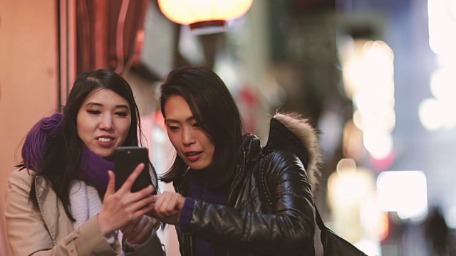 日本东京新宿，日本女性朋友晚上看智能手机视频素材