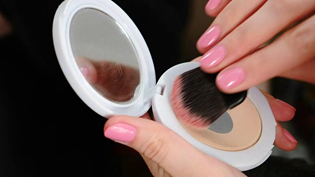 特写女人的手化妆粉和镜子用刷子化妆。视频素材