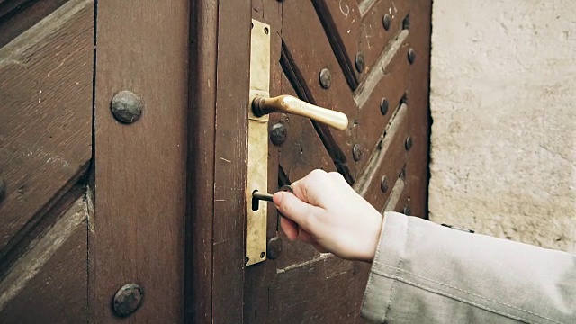 女手用旧钥匙打开旧门。手把一个古董铁钥匙在门锁和手转动钥匙。视频素材