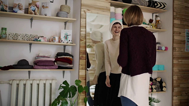 快乐的女人在纺织车间的镜子前试穿针织帽视频下载