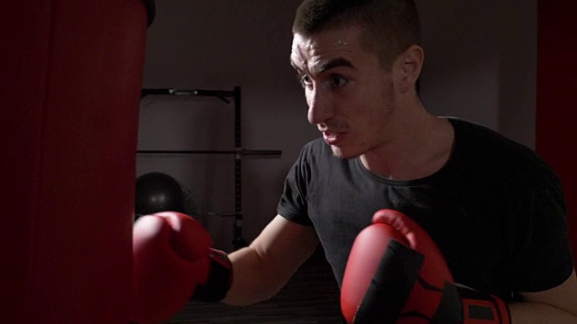 侧面的年轻运动拳击手戴红色拳击手套和打击沙袋紧张的慢动作视频素材