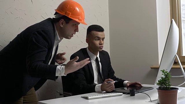 两个年轻的商人兼建筑师在办公室里讨论项目并看着显示器。建筑商、工程师、概念。60 fps视频下载