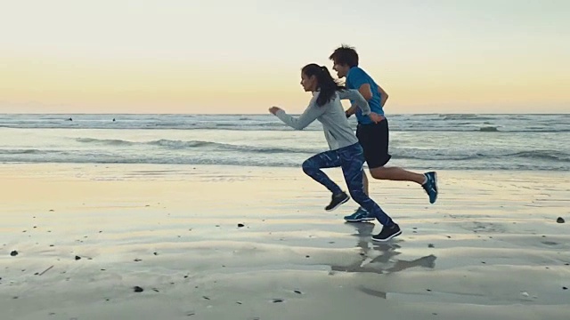 日落时分，健康的情侣在海滩上进行慢动作训练视频素材