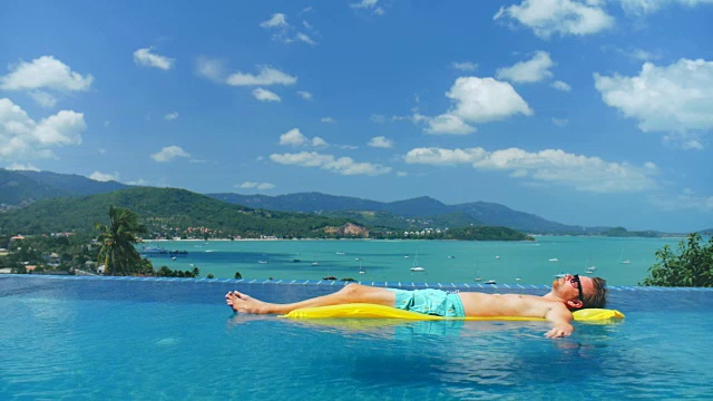 放松男人在蓝色短裤漂浮在床垫上的水游泳池视频下载