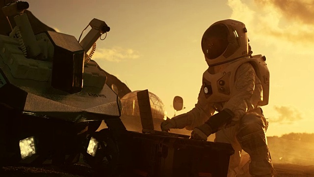宇航员穿着宇航服在一台笔记本电脑上工作，在一个新的外星红色星球/火星上调整火星车。日光高科技太空探索，可居住行星的发现，殖民。视频下载