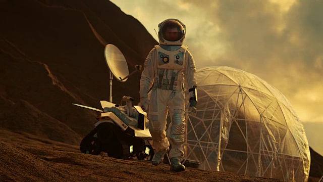 穿着太空服的宇航员行走在红色星球/火星上。背景是他的基地/研究站，附近停着火星车，炽热的阳光照耀着他。视频下载