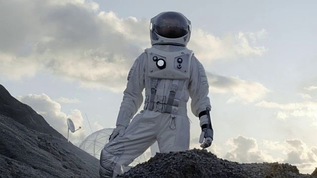 宇航员站在寒冷的外星山上环顾四周。背景:他的基地/研究站。科技的进步带来了太空探索和殖民。视频素材