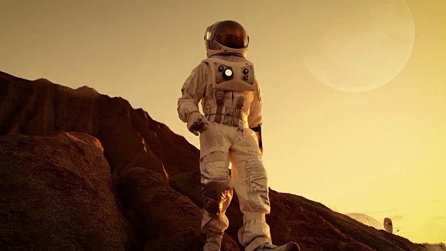 勇敢的宇航员从外星红色星球/火星的山上降落。太空探索/旅行，殖民概念。视频下载