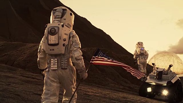 下面是两位宇航员探索火星/红色星球的照片。一名宇航员举着美国国旗。科技的进步带来了太空探索、旅行和殖民的概念。视频素材
