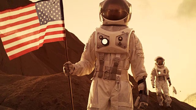 两名宇航员探索火星/红色星球。一名宇航员举着美国国旗。科技的进步带来了太空探索、旅行和殖民的概念。视频素材