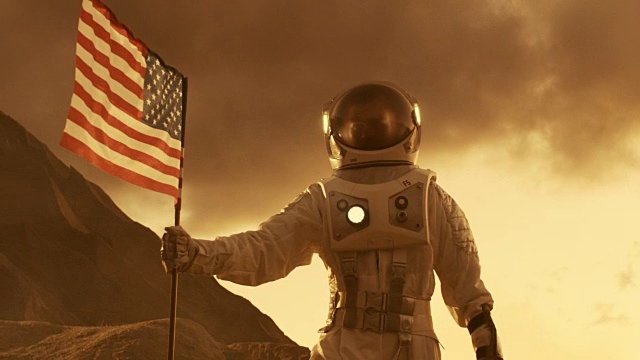 强壮的宇航员在火星上行走，带着美国国旗，自豪地把它种在红色星球的表面。太空旅行，殖民主题。视频素材