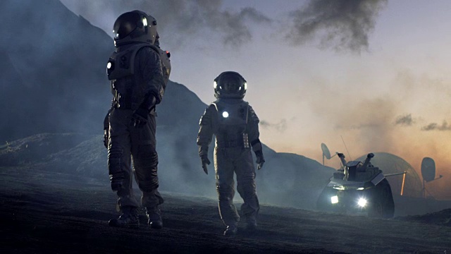 两名宇航员穿着宇航服，自信地在外星行走，探索星球表面。在背景研究基地/站和漫游者。太空旅行，殖民概念。视频下载