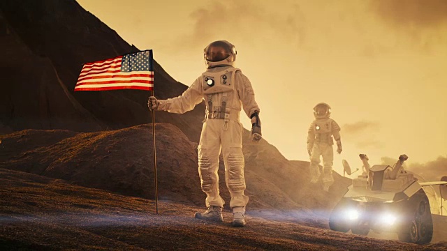 两名宇航员探索火星/红色星球。一名宇航员举着美国国旗。科技的进步带来了太空探索、旅行和殖民的概念。视频素材