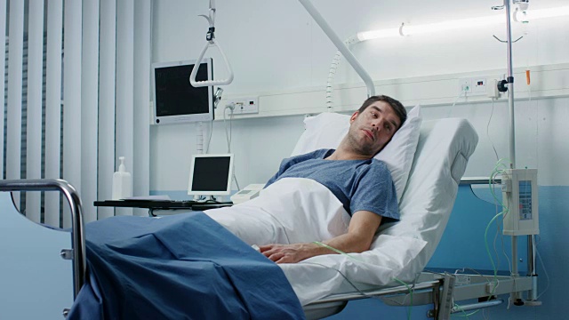 一个重病人躺在医院的病床上。监视器显示了他的生命体征。病房是干净的和新的。视频素材