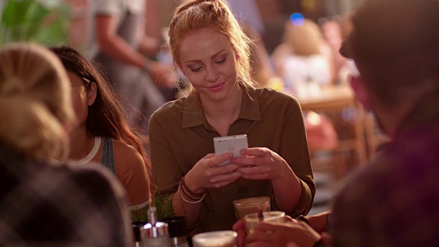 一个年轻女子在咖啡厅和朋友们用手机发短信视频素材