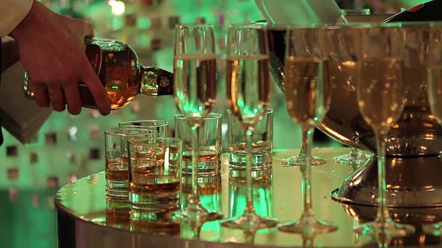 自助餐桌上放着一杯香槟和葡萄酒，桶里装着一瓶香槟或葡萄酒，背景是人们在跳舞，模糊的剪影视频下载
