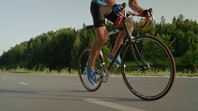 低角度:年轻男性骑自行车沿着空旷的柏油路，经过镜头。视频素材
