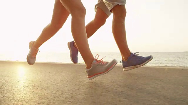低角度，近:适合夫妇跑在阳光明媚的沥青海洋道路在夏天。视频素材