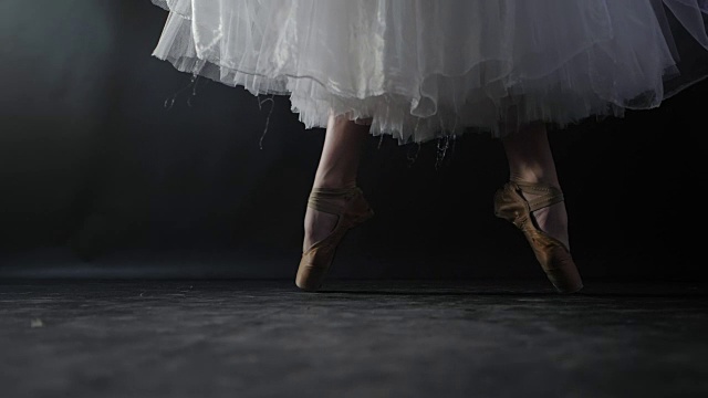 芭蕾舞演员的特写，因为她在黑暗的舞台或工作室练习。穿尖头鞋的女人的脚。芭蕾舞女演员表演经典芭蕾舞剧。缓慢的运动。耀斑,常平架视频素材