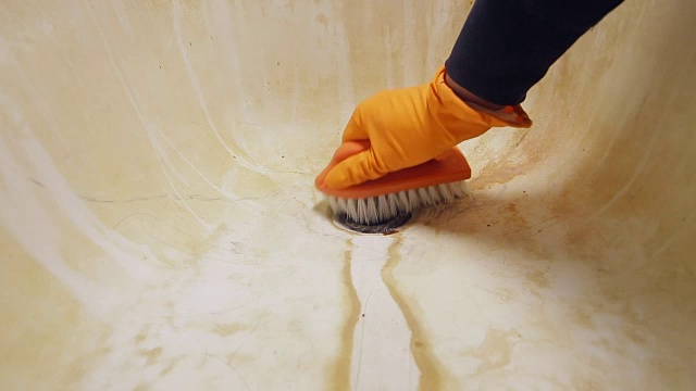 一个戴着橙色橡胶手套的男人的手正在用刷子清洁浴缸的水槽。一般打扫屋子视频素材