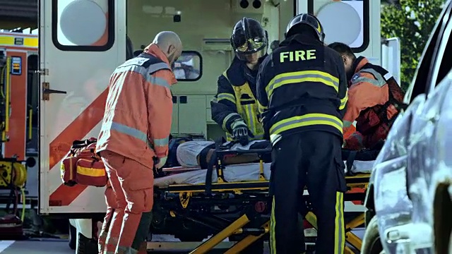 在消防队员的帮助下，医护人员将一名伤者用担架抬上救护车视频下载