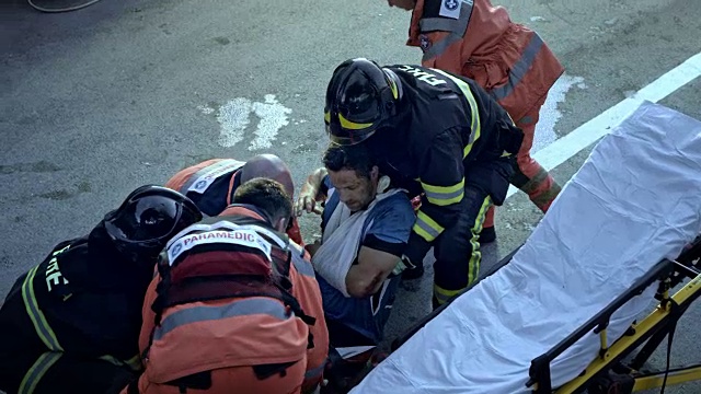 在事故现场，消防员和医护人员将受伤的男性自行车手抬到担架上视频下载