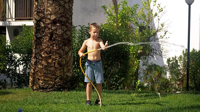 男孩试图应付水射流时，给草坪浇水视频素材