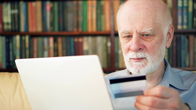 留胡子的帅老头坐在家里。在笔记本电脑上用信用卡网上购物视频素材